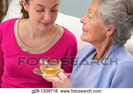 senior woman in a mauve cardigan, and young help giving her a cup of tea at home View Large Photo Image Stock Photo - senior woman in a mauve cardigan, and young help giving her a cup of tea at home. Fotosearch