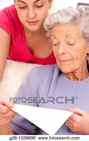 senior woman in a mauve cardigan, and young person who helps her reading papers at home View Large Photo Image Stock Photograph - senior woman in a mauve cardigan, and young person who helps her reading papers at home. Fotosearch