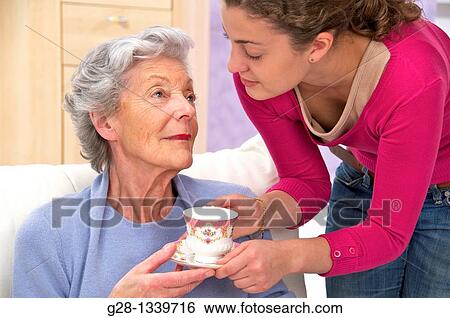 senior woman in a mauve cardigan, and young help giving her a cup of tea at home View Large Photo Image Stock Photograph - senior woman in a mauve cardigan, and young help giving her a cup of tea at home. Fotosearch