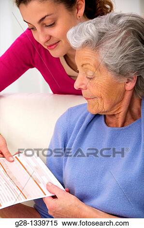 senior woman in a mauve cardigan, and young person who helps her reading medical papers at home View Large Photo Image Stock Photography - senior woman in a mauve cardigan, and young person who helps her reading medical papers at home. Fotosearch