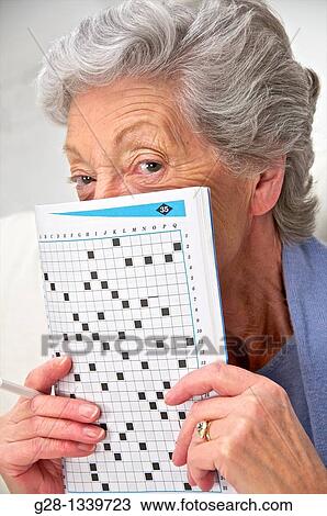 senior woman in a mauve cardigan, holding a crosswords magazine in front of her at home View Large Photo Image Stock Image - senior woman in a mauve cardigan, holding a crosswords magazine in front of her at home. Fotosearch