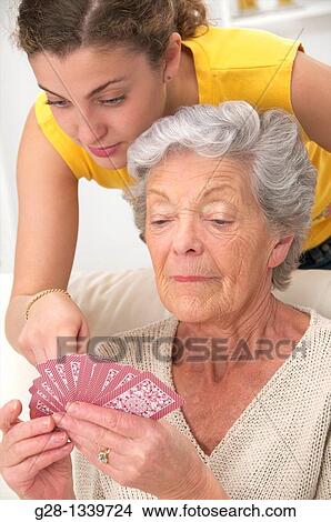 Picture - senior woman in beige playing cards with a young woman who helps her at home. Fotosearch