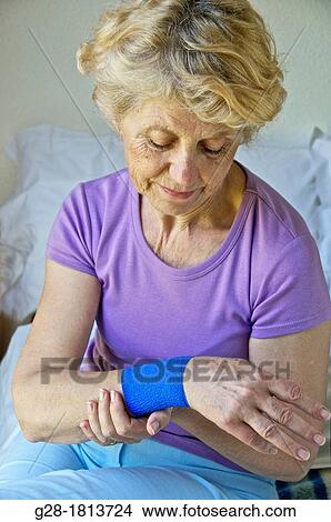 Senior woman in mauve, sitting on her bed, Holding her wrist with a blue bandage on it View Large Photo Image Picture - Senior woman in mauve, sitting on her bed, Holding her wrist with a blue bandage on it. Fotosearch