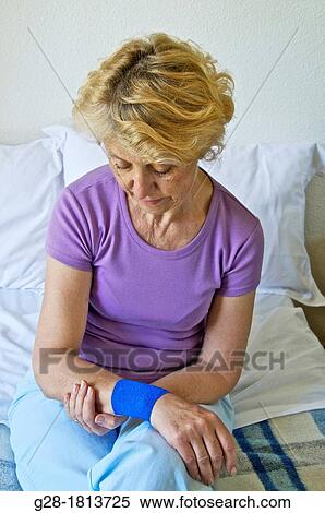 Senior woman in mauve, sitting on her bed, Holding her wrist with a blue bandage on it View Large Photo Image Stock Photography - Senior woman in mauve, sitting on her bed, Holding her wrist with a blue bandage on it. Fotosearch