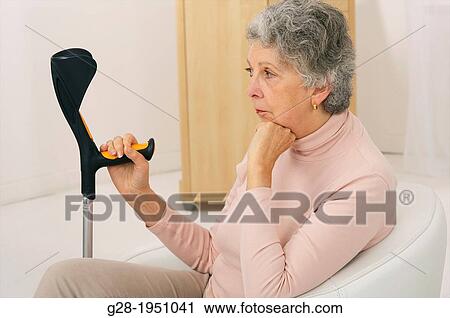 Stock Image - Senior woman in pink holding a walking stick and waiting sitting in an armchair. Fotosearch