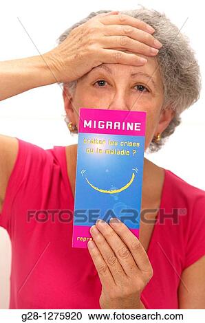 Stock Image - senior woman in pink, suffering from a headache and holding a medical leaflet on headache migraine. Fotosearch