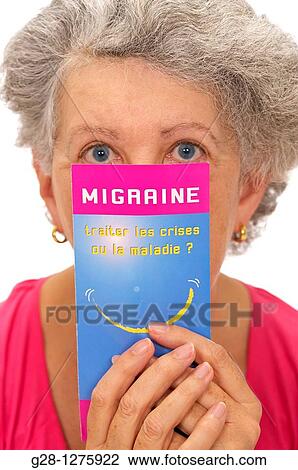 Stock Image - senior woman in pink, suffering from a headache and holding a medical leaflet on headache migraine. Fotosearch