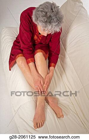 Senior woman in red, putting her hands on her legs and ankle to relieve pain of a sprained ankle View Large Photo Image Stock Photography - Senior woman in red, putting her hands on her legs and ankle to relieve pain of a sprained ankle. Fotosearch
