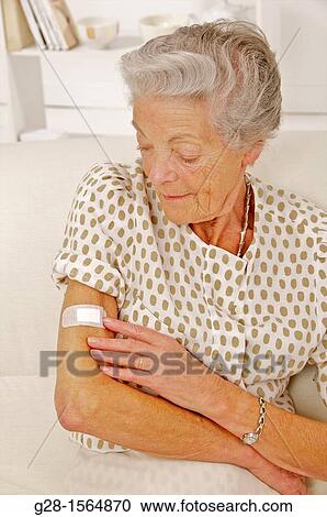Stock Image - Senior woman looking at a dressing on her arm. Fotosearch