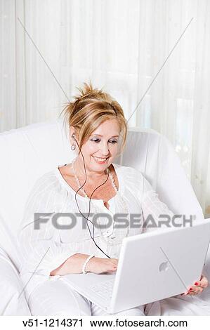 Stock Image - Senior woman on the couch with laptop and listening to music. Fotosearch