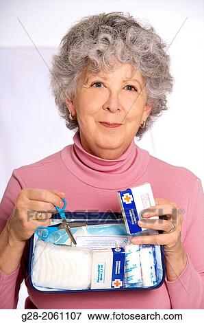 Senior woman, or senior nurse, in pink, holding transparent plastic first aid kit in her hands with blue scissors and dressings, at home or in surgery View Large Photo Image Stock Photo - Senior woman, or senior nurse, in pink, holding transparent plastic first aid kit in her hands with blue scissors and dressings, at home or in surgery. Fotosearch