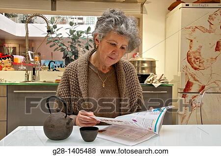 Senior woman reading a magazine and drinking a cup of tea in her kitchen View Large Photo Image Stock Photo - Senior woman reading a magazine and drinking a cup of tea in her kitchen. Fotosearch