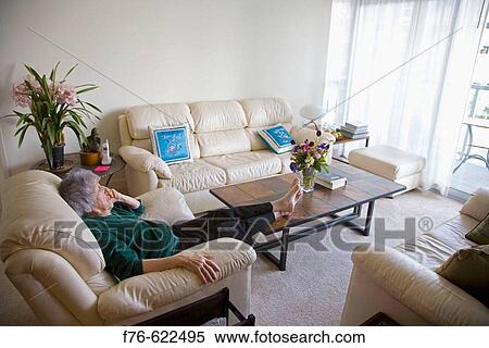 Stock Photography - Senior woman relaxing with feet up on coffee table in bright apartment.. Fotosearch