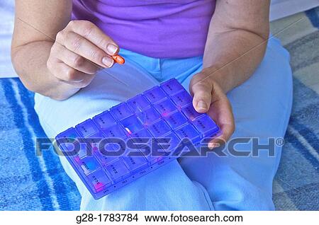 Senior woman? s hands, one holding a medical capsule between 2 fingers, the other holding a daily drug distributor, close up View Large Photo Image Picture - Senior woman? s hands, one holding a medical capsule between 2 fingers, the other holding a daily drug distributor, close up. Fotosearch