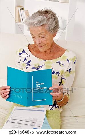 Stock Photography - Senior woman sitting and reading instructions in a retirement guide book. Fotosearch