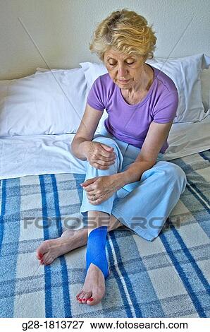 senior woman sitting on her bed, and holding her leg with a blue bandage around her twisted ankle View Large Photo Image Stock Photo - senior woman sitting on her bed, and holding her leg with a blue bandage around her twisted ankle. Fotosearch