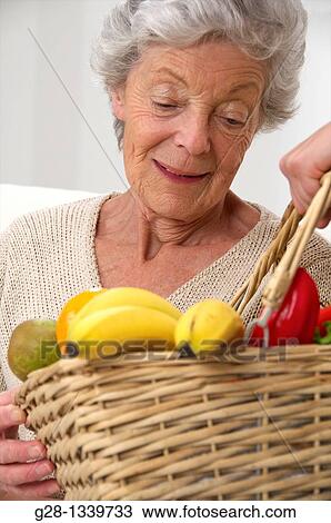 senior woman smiling and looking at a basket full of fruits which is offered to her View Large Photo Image Stock Image - senior woman smiling and looking at a basket full of fruits which is offered to her. Fotosearch