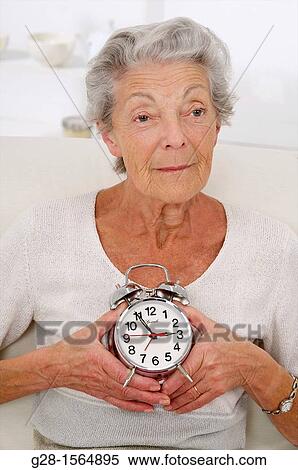 Senior woman thoughtful holding an alarm clock View Large Photo Image Stock Photography - Senior woman thoughtful holding an alarm clock. Fotosearch