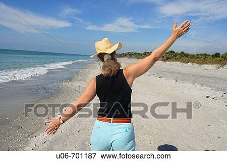 Stock Photo - Senior woman walking at Casperson Beach in Venice (Florida, USA) with arms wide open. Fotosearch