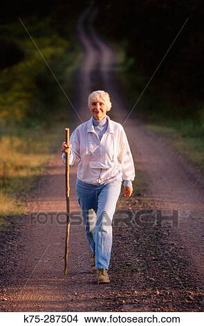 Picture - Senior woman walking country road. Fotosearch