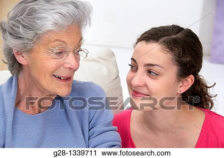 senior woman wearing glasses and a mauve cardigan smiling with a young woman at her side at home View Large Photo Image Stock Image - senior woman wearing glasses and a mauve cardigan smiling with a young woman at her side at home. Fotosearch