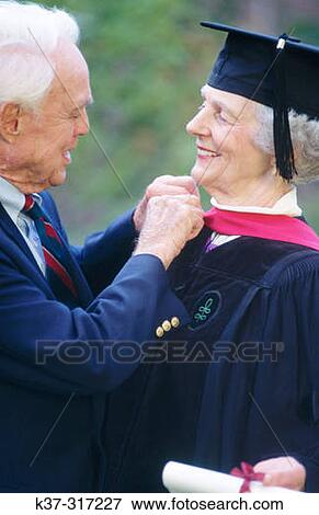 Senior woman wearing graduation cap and gown being congratulated by her husband on receiving college degree View Large Photo Image Stock Photo - Senior woman wearing graduation cap and gown being congratulated by her husband on receiving college degree. Fotosearch