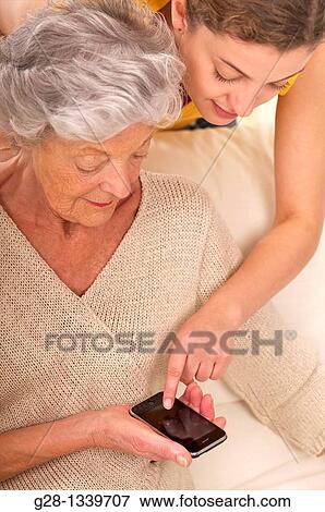 senior woman with a young woman who helps her using a portable phone View Large Photo Image Stock Photo - senior woman with a young woman who helps her using a portable phone. Fotosearch