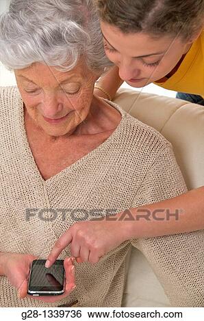 senior woman with a young woman who helps her using a portable phone View Large Photo Image Stock Photograph - senior woman with a young woman who helps her using a portable phone. Fotosearch