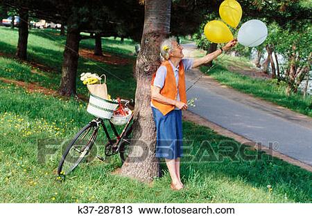 Senior woman with bike and balloons in park View Large Photo Image Stock Image - Senior woman with bike and balloons in park. Fotosearch