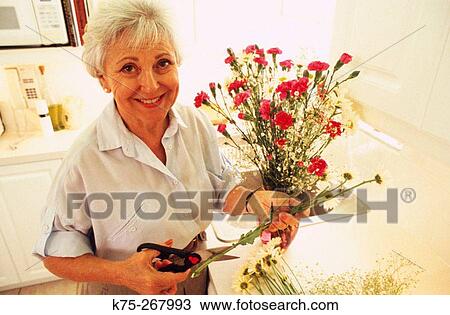 Stock Image - Senior woman with bouquet of flowers in kitchen. Fotosearch