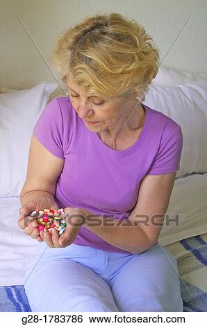 Senior womann holding a handful of colored pills and capsules in her hands, sitting on her bed in her bedroom View Large Photo Image Stock Photograph - Senior womann holding a handful of colored pills and capsules in her hands, sitting on her bed in her bedroom. Fotosearch