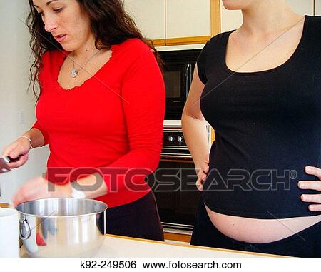 Stock Photograph - Seven-month pregnant woman and her best friend cooking. Fotosearch