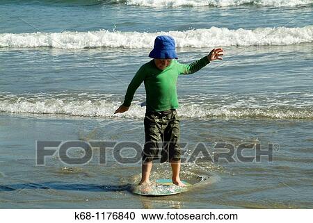 Stock Image - seven year old boy playing with a skim board on the beach near Tofino, West Coast, Vancouver Island, British Columbia, Canada. Fotosearch