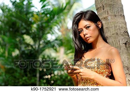 Stock Image - Sexy young woman, leaning against tree, Indonesia, Asia. Fotosearch
