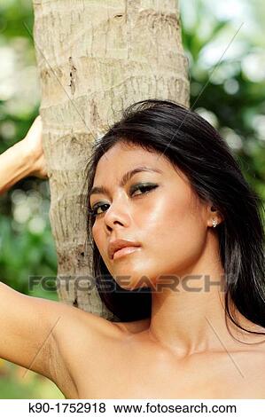 Stock Photo - Sexy young woman, leaning at tree trunk, Indonesia, Asia. Fotosearch