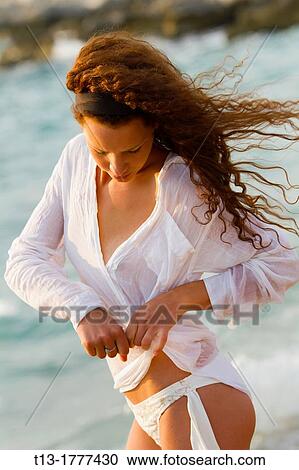 Stock Image - Sexy young woman on the beach tying a shirt. Fotosearch