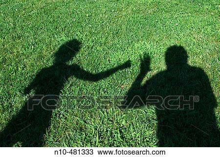 Stock Image - Shadow on the grass at a park of two people pretending to be fighting. Fotosearch