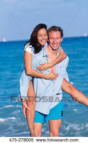 She rides piggyback at the beach View Large Photo Image Stock Photography - She rides piggyback at the beach. Fotosearch