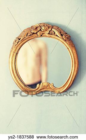 Stock Photo - Shirtless adult male reflected in antique mirror hanging on wall. Fotosearch