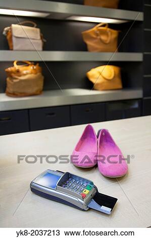 Stock Image - Shoes on clerk desk in retail shop. Card reader and bags or shoulder bags. Pricing, debit machine, counter.. Fotosearch