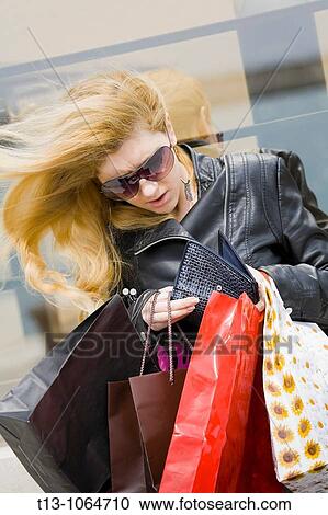 Stock Image - Shopping rush, pretty young woman is looking into her wallet and the wind is blowing her long blonde hair. Fotosearch