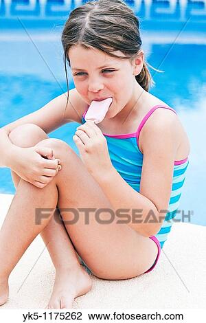 Stock Image - Shot of a Cute Blonde Girl On Holiday by the Pool Eating an Ice Lolly. Fotosearch