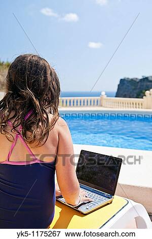 Stock Photo - Shot of a Young Girl in Swimsuit Using her Laptop by the Pool. Fotosearch