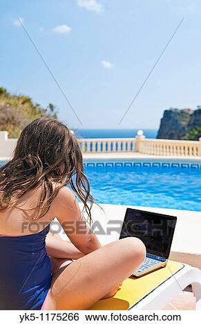 Stock Photograph - Shot of a Young Girl in Swimsuit Using her Laptop by the Pool. Fotosearch