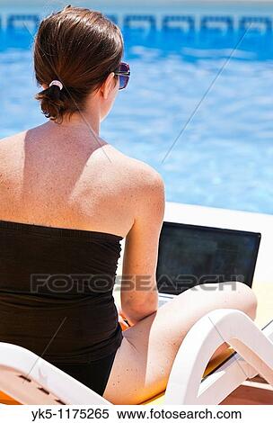 Stock Photography - Shot of a Young Woman in Swimsuit Using her Laptop by the Pool. Fotosearch