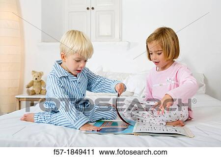 Stock Image - Siblings reading a book in their pyjamas. Fotosearch