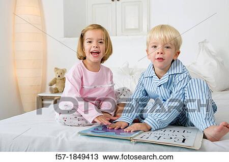 Stock Image - Siblings reading a book in their pyjamas. Fotosearch