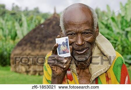 Sidama Tribe Ethiopia Africa old man age 82 with his hut home and holding new Fuji Polaroid photo print 30 View Large Photo Image Stock Image - Sidama Tribe Ethiopia Africa old man age 82 with his hut home and holding new Fuji Polaroid photo print 30. Fotosearch