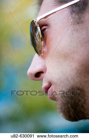 Stock Image - Side view of a young man wearing sunglasses, focus on eyes.. Fotosearch