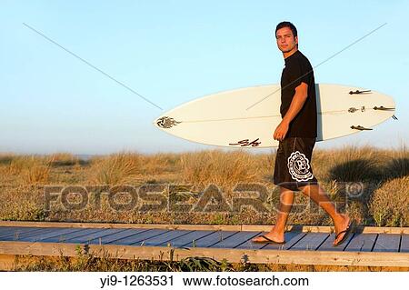 Side view of man walking along ocean carrying surf board View Large Photo Image Stock Image - Side view of man walking along ocean carrying surf board. Fotosearch